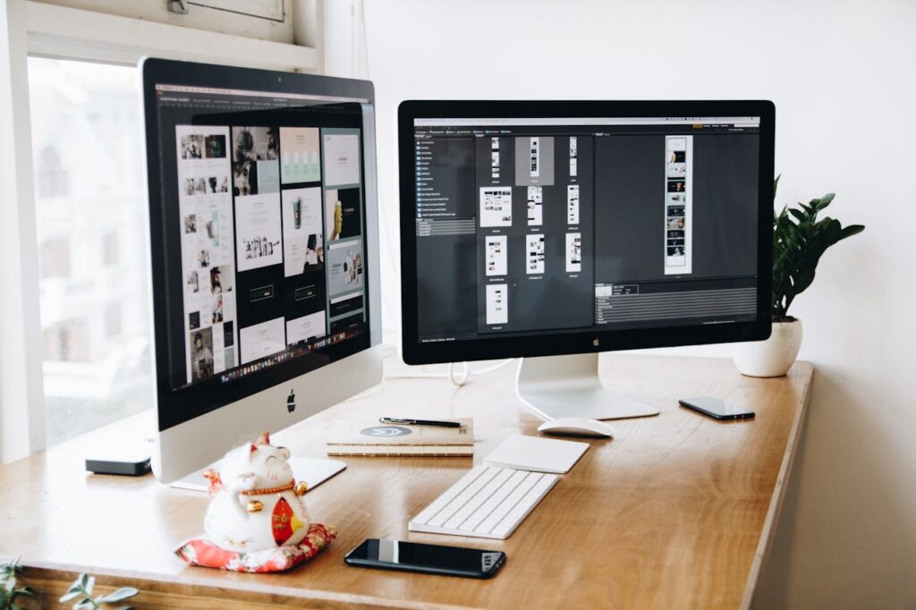 Two Imac's With Keyboard and Phones on Desk with web designs on screen.