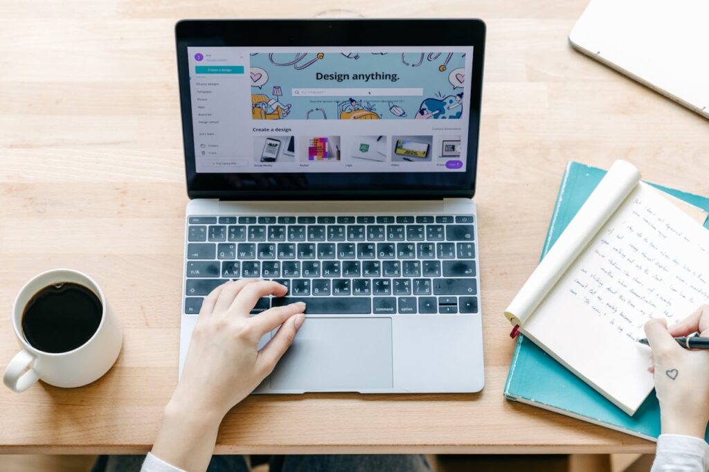 laptop on a wooden desk with notepad to the right and coffee cup to the left