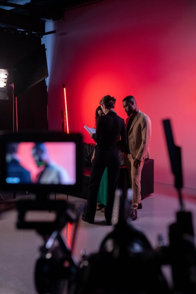 Group of People Standing on red lighted set Looking at the Script with camera pointed at them.